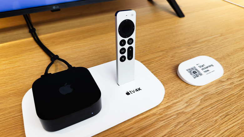 Apple TV 4K box with its remote placed on a white base on a wooden desk