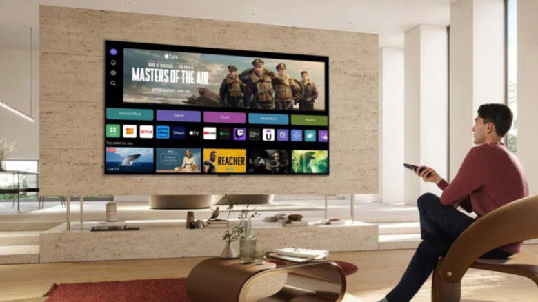 A man pointing a remote at a wall-mounted LG TV.