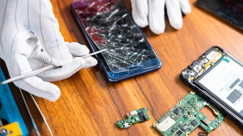A repair technician lifts a cracked screen protector off a phone.