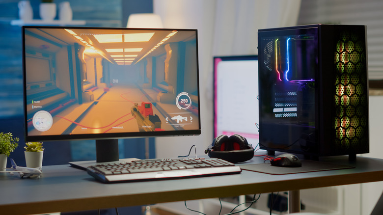 a monitor displaying an old school shooter on a desk next a computer and gaming peripherals