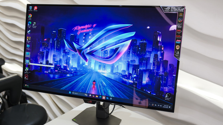 a 240Hz gaming monitor showing home screen and brand/specs on a sticker while standing on a desk