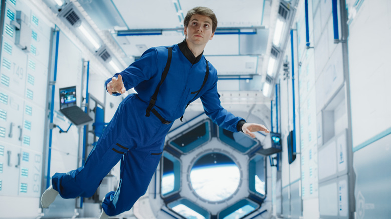 A male astronaut working aboard a spacecraft. He's hovering in midair.