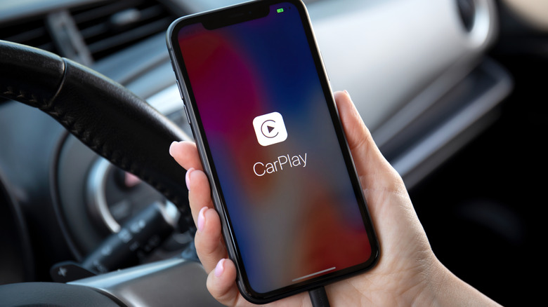 A person holding an iPhone with Apple CarPlay icon on the screen