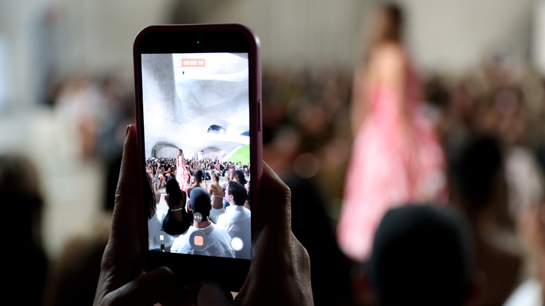 A person holds up their phone to shoot a fashion show catwalk.
