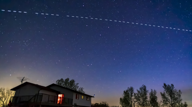 a line of Starlink satellites passing through the sky over a house
