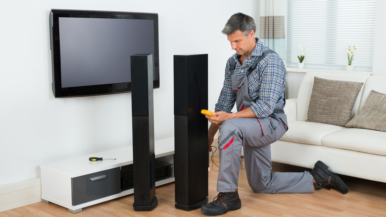A man uses a multimeter to check a tower speaker in a minimalist living room.