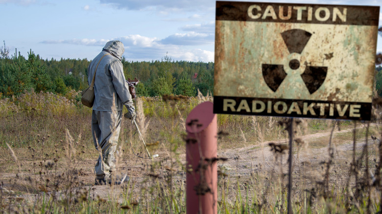 A person measures radiation in a containment zone in front of an old caution sign
