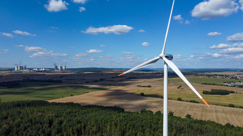 A wind turbine above a field with a nuclear plant in the background
