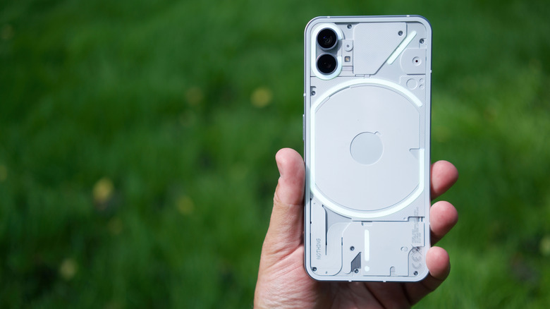 Close-up of a person holding the Nothing Phone (1) with blurred grass in the background