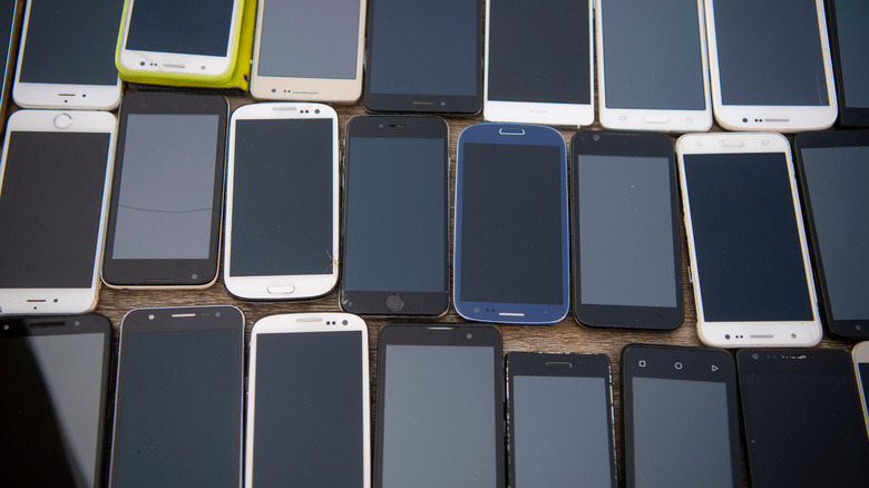 Lots of old touchscreen devices lined up on a table with screens off.