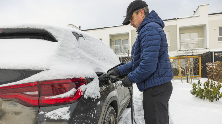 A man charging his EV in a snowy area.