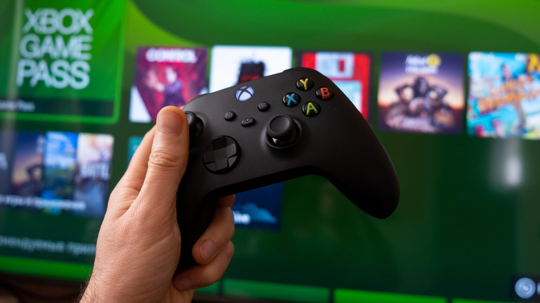 Someone holding a standard Xbox controller in front of a TV with the Xbox UI visible.