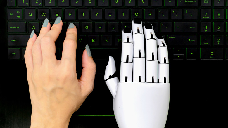 Human hand and robot hand on a keyboard next to each other.