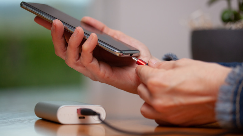 USB C cord plugged into smartphone from power bank to charge.