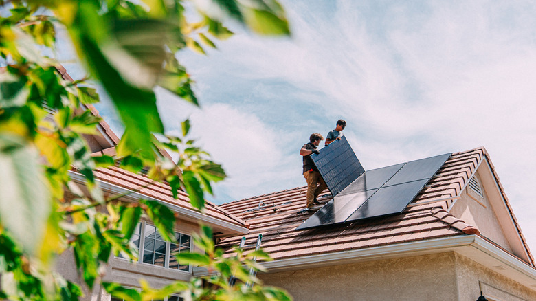 Two workers installing solar panels on a residential home
