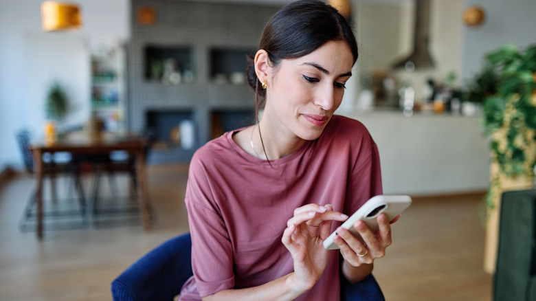 A woman sitting on a chair tapping her phone.