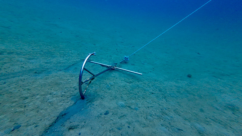A ship's anchor on the seafloor under the surface tied to a vessel.