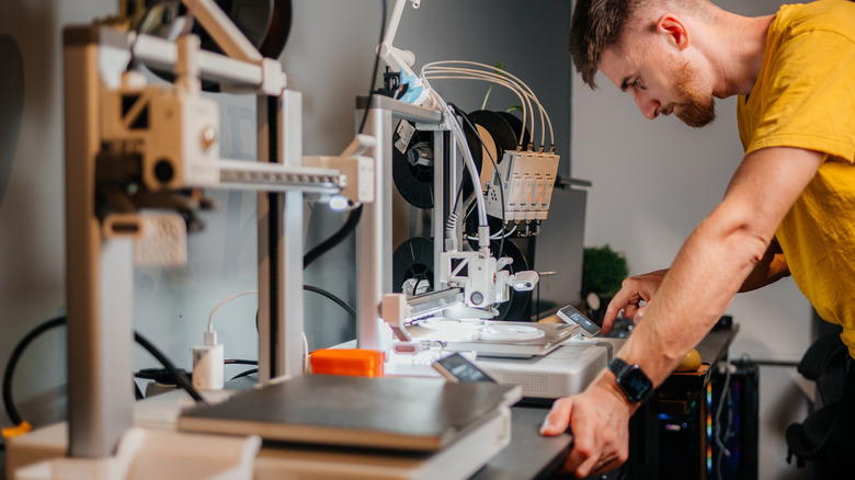 Young man looking over his 3D printer settings with machines visible.