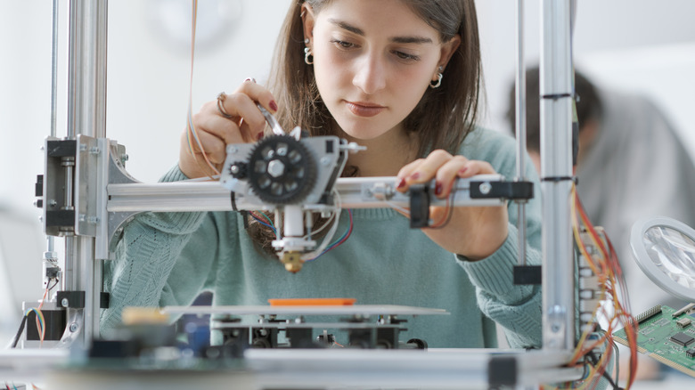 Young woman doing maintenance on a 3D printer in a lab setting.