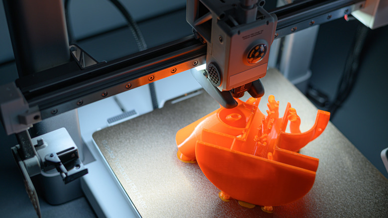 A 3D printer at work printing a small orange model