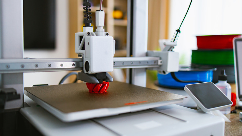 A 3D printer at work printing a small red widget