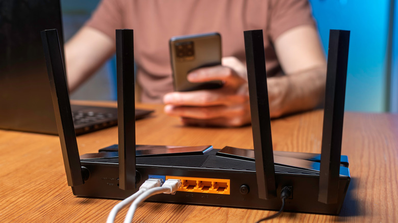 Modern Wi-Fi router on desk with user and mobile device and laptop in background.