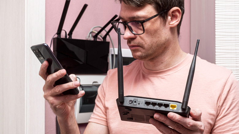 Man holding a wireless router in one hand and a mobile device in the other.