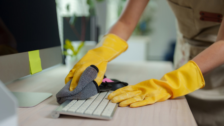 Person wearing cleaning gloves cleaning keyboard with microfiber cloths