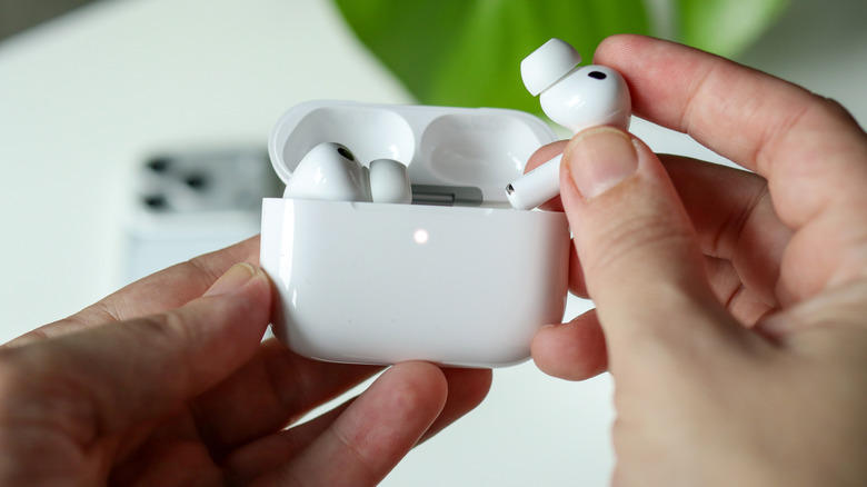 A hand holding AirPods in their case, one bud outside of the case.