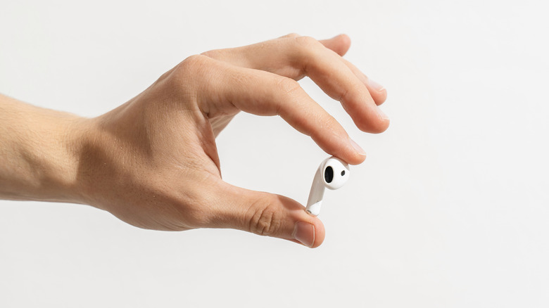 A hand holding a single wireless earbud on a white background.