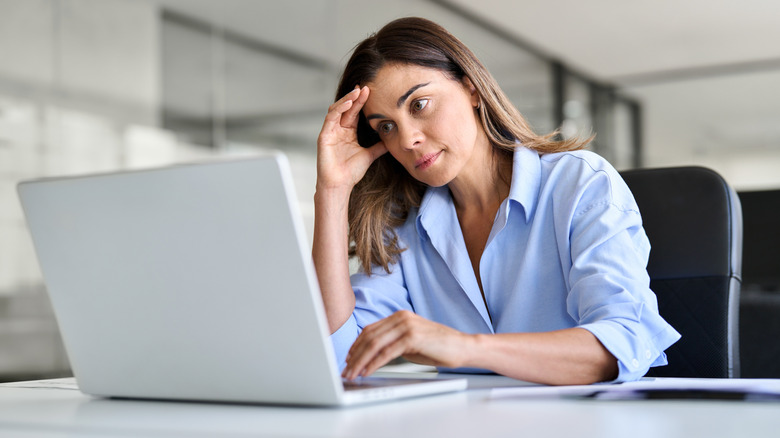 A worried-looking woman looking at a laptop.