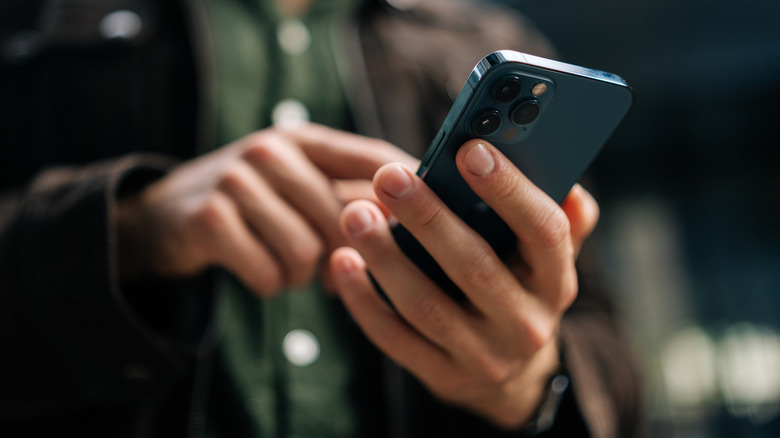 Close-up shot of a man holding a smartphone with one hand while using the screen