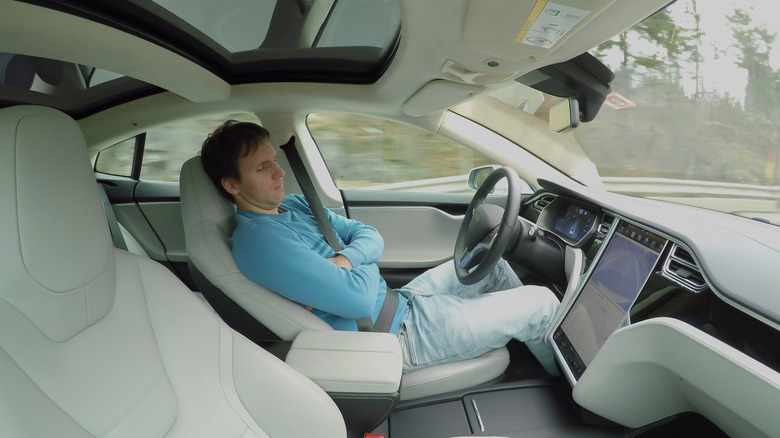 Man resting behind the wheel of an EV that's driving autonomously