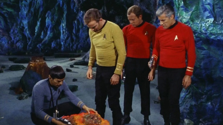 Kirk and two red shirts looking at Spock examining a rock in Star Trek