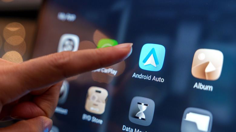 Finger moving toward Android Auto icon on a car's smart display