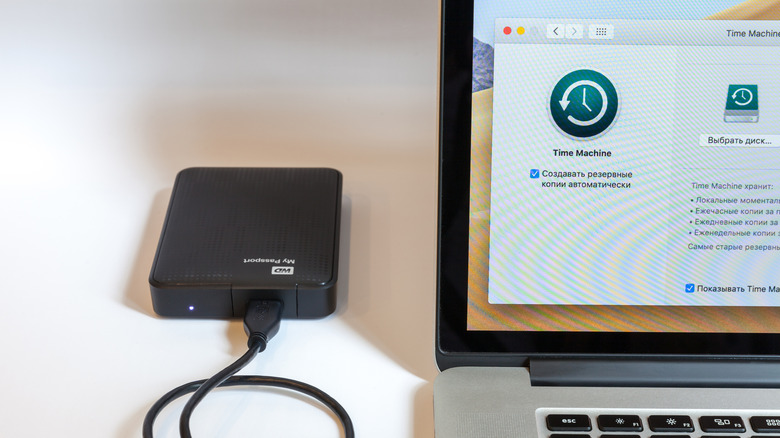 Open MacBook, on-screen program Time Machine. An external hard drive is connected to the MacBook.