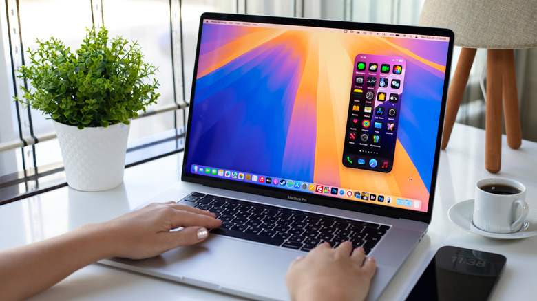 Woman hand holding Apple Macbook Pro and iPhone 15 Pro Max Mirroring with home screen AI Apple Intelligence
