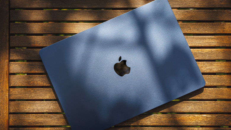 New MacBook Air laptop with M4 chip and visible Apple logo in midnight color placed on wooden table outdoors