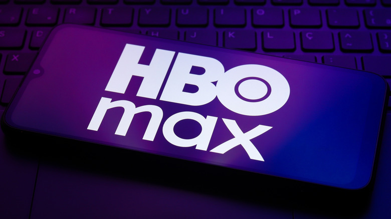 The HBO Max app logo appears on the screen of a smartphone