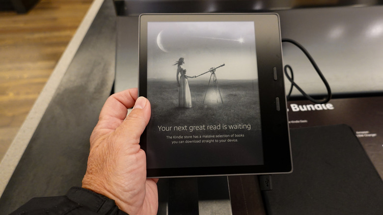 A person holding a store display version of the Kindle Oasis.