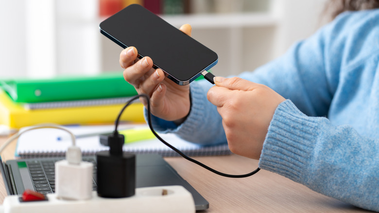 Someone plugging their phone into a charger which is connected to a power strip.