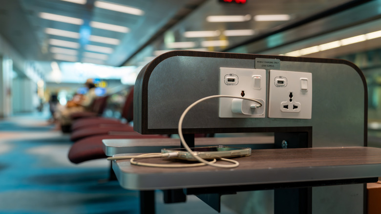USB charging station in an airport with a phone plugged in.