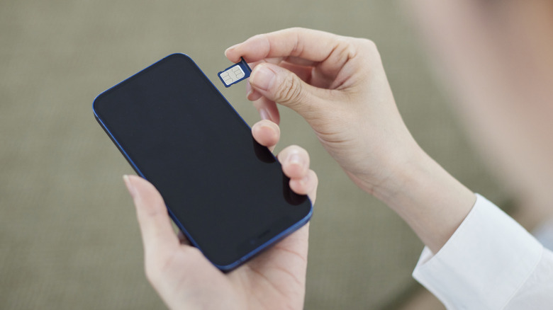 A woman holding a smartphone as she prepares to put the SIM card into it