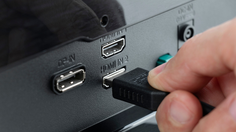 Close-up of a hand connecting an HDMI cable to the back of a monitor