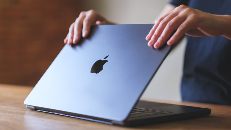 A person closing a MacBook laptop