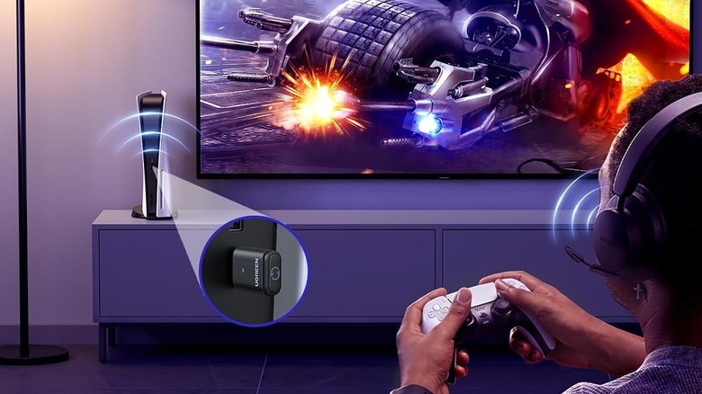 A UGREEN USB adapter is plugged into a PS5 on top of a TV stand. A gamer plays a game on a wall-mounted TV.