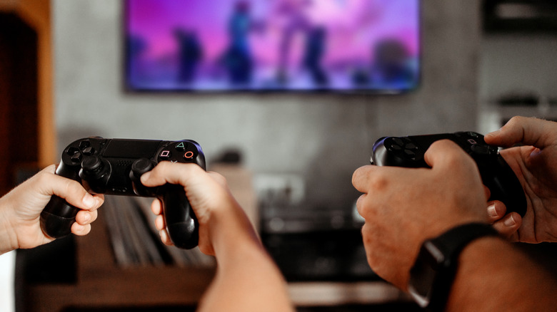 Two pairs of hands holding PlayStation controllers