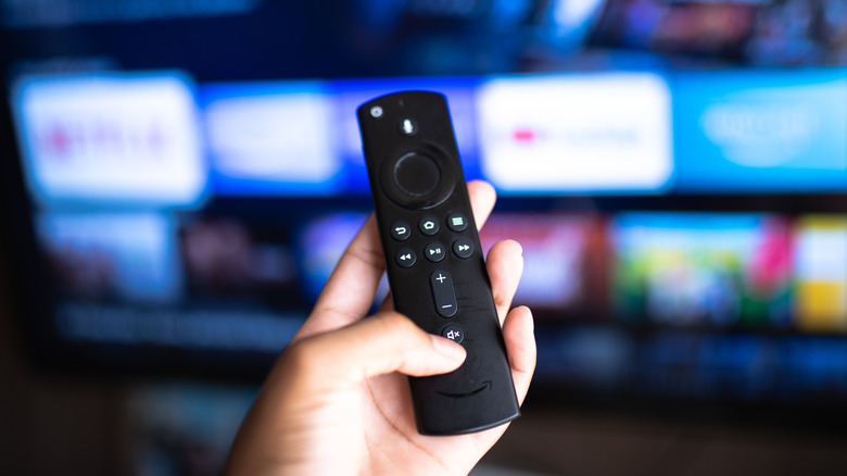A person holding a Fire TV Stick remote with a TV in background