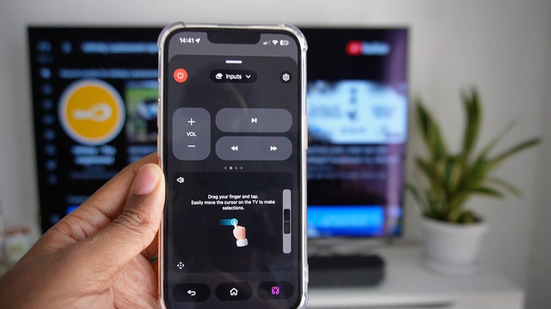Hand holding iPhone with ThinQ app controlling LG TV