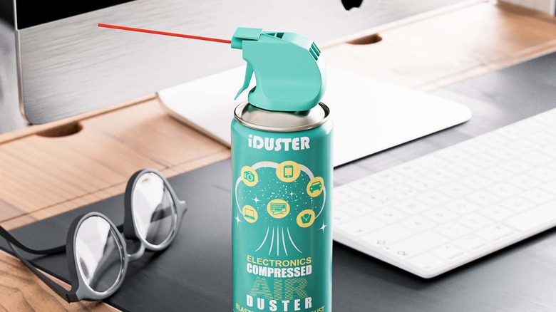 A can of iDuster compressed air in front of a Mac computer and a pair of glasses on a desk